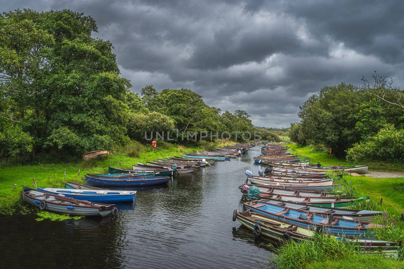 Wooden paddle boats or motor boats moored in row on river or canal surrounded by lush green trees near Lough Leane, Ring of Kerry, Killarney, Ireland