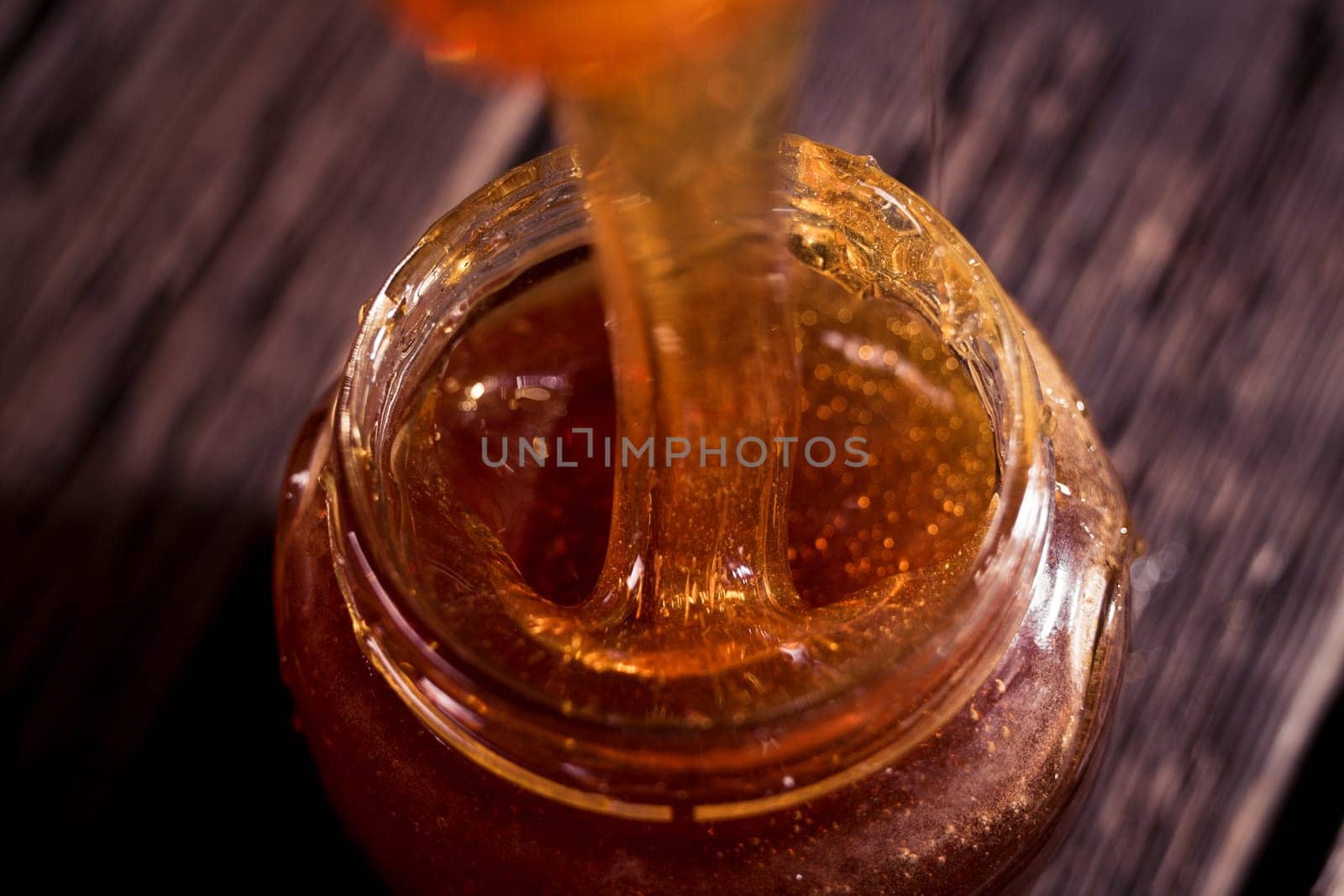Honey dripping from a wooden honey dipper   on black background