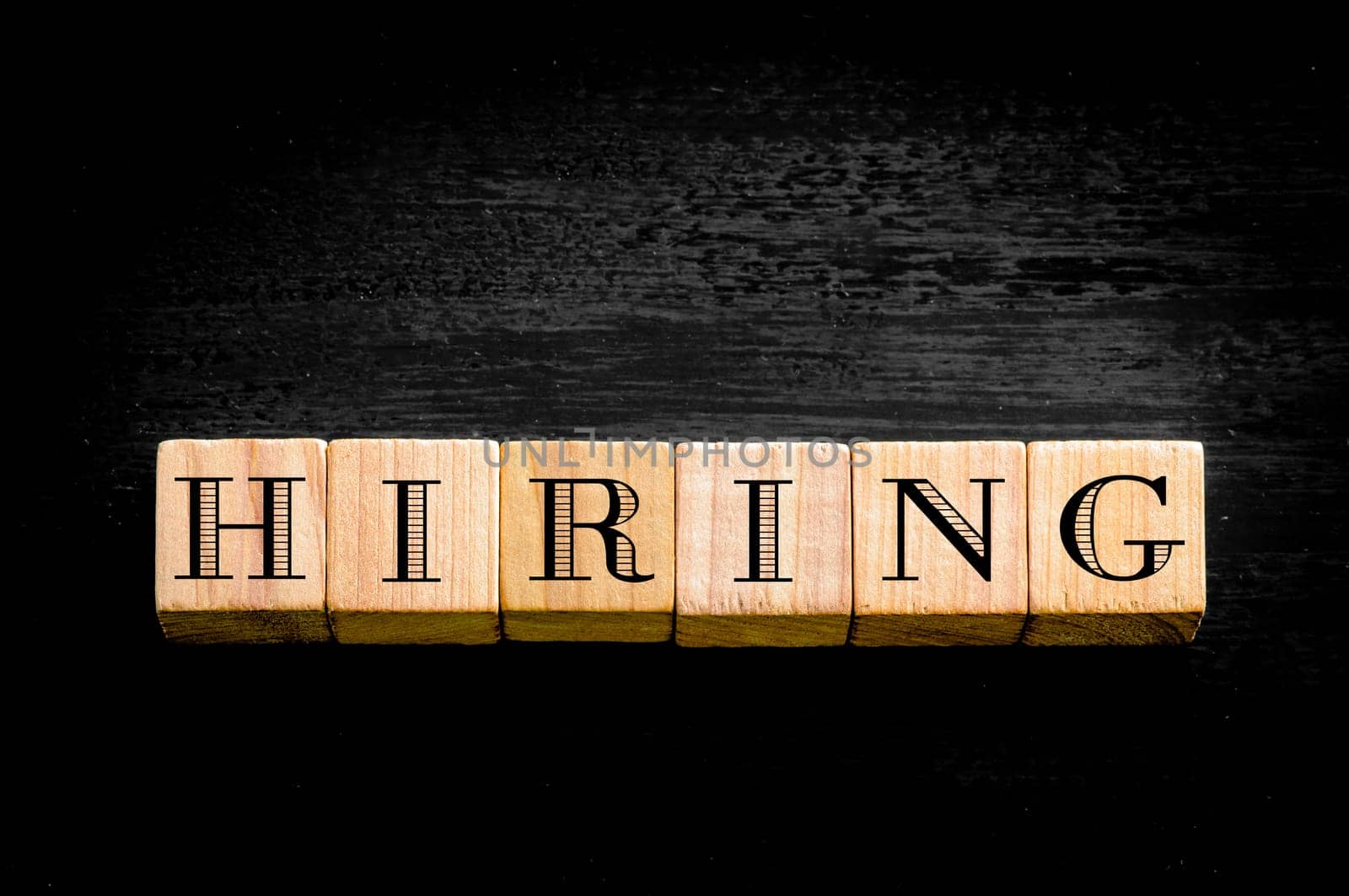 Word Hiring. Wooden small cubes with letters isolated on black background.Concept image.