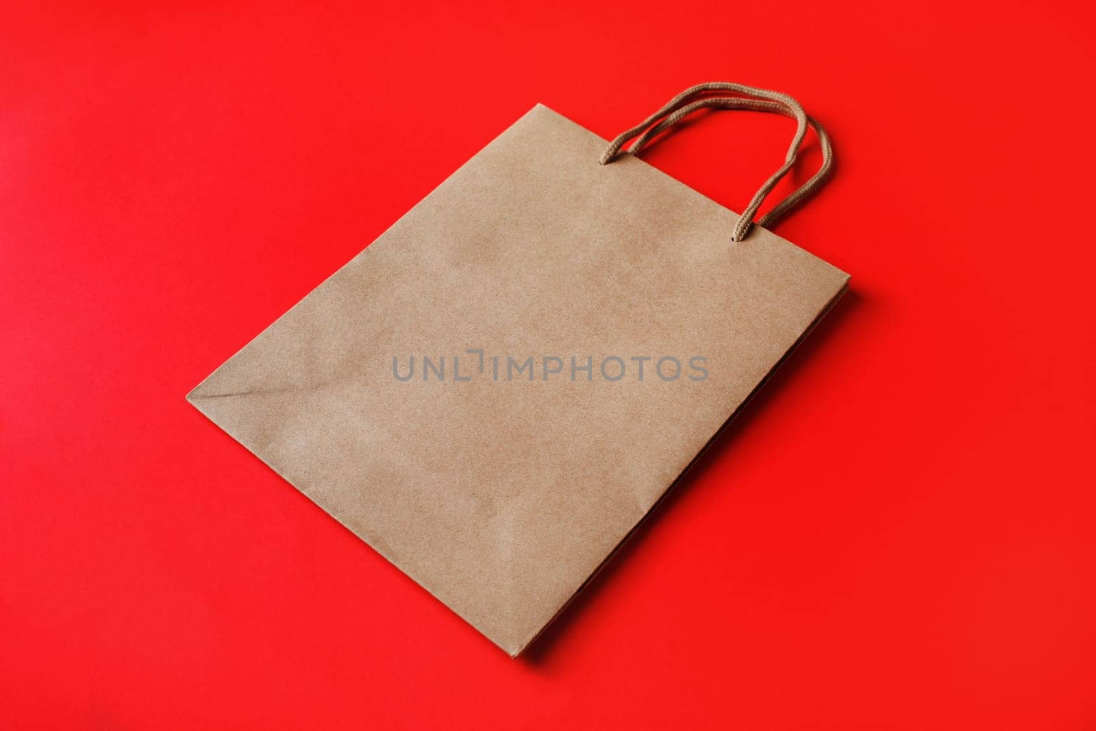 Brown paper bag with handles on red paper background.