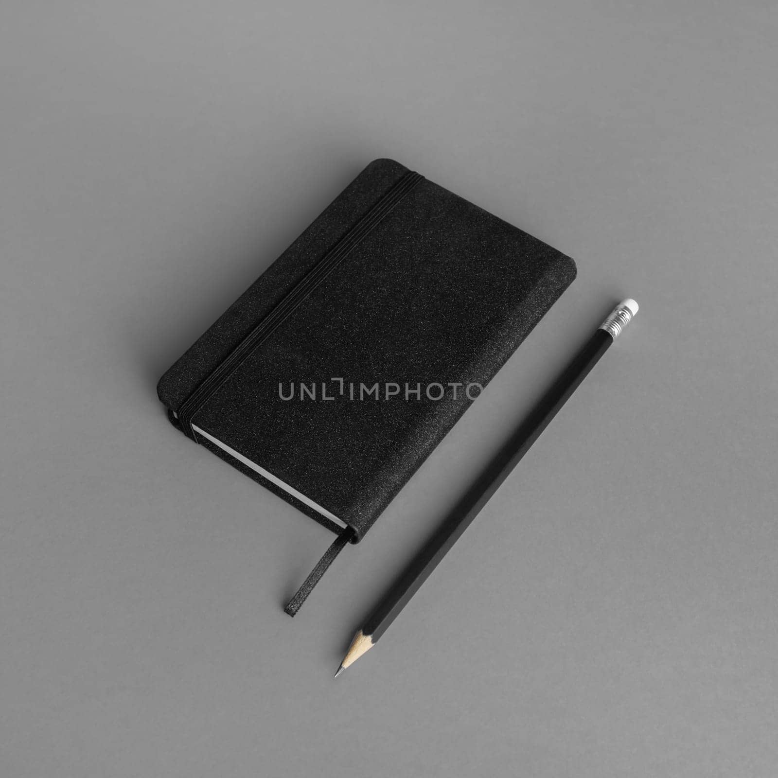 Blank black notepad and pencil on gray paper background.