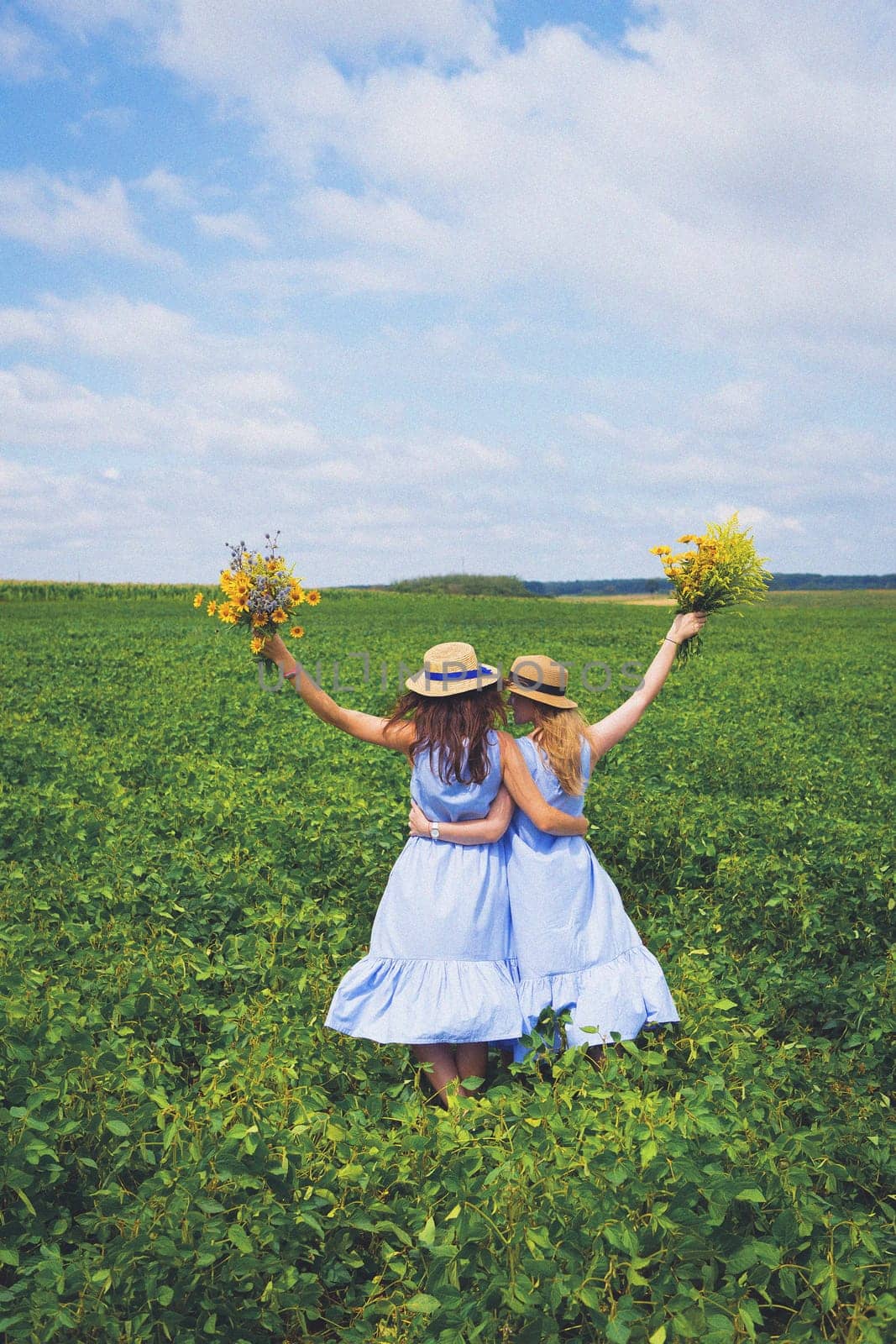 Two beautiful girlfriends in hats hugging in a green field, a postcard under the old-fashioned.
