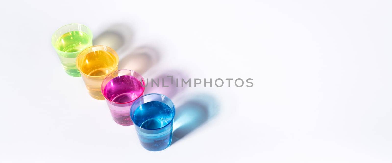 Plastic multi-colored glasses with liquid on a white background with highlights. Layout, mockup.