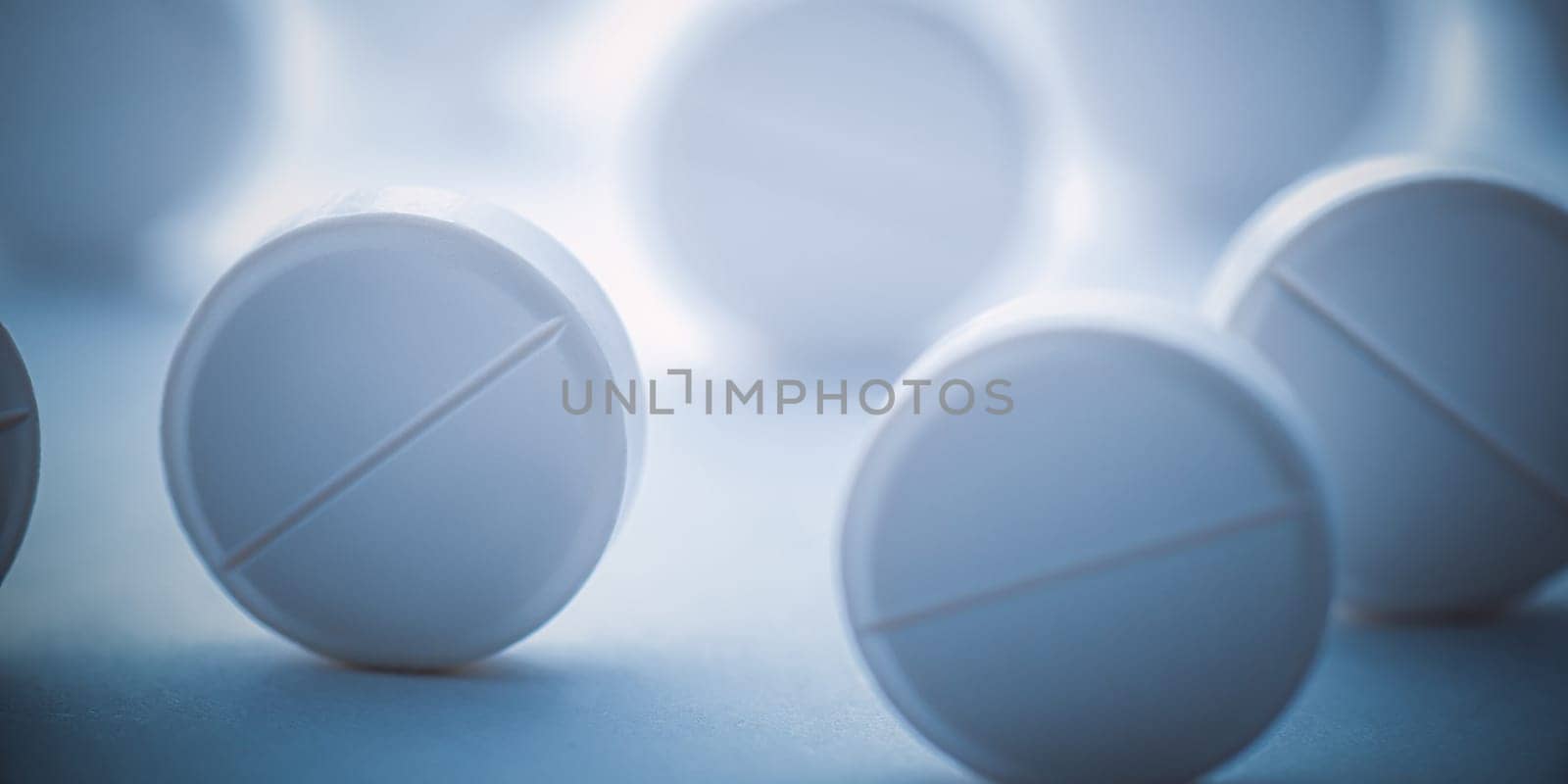 A pile of white pills scattered on a white background with blue tinting. Selective focus. Mockup layout, template.