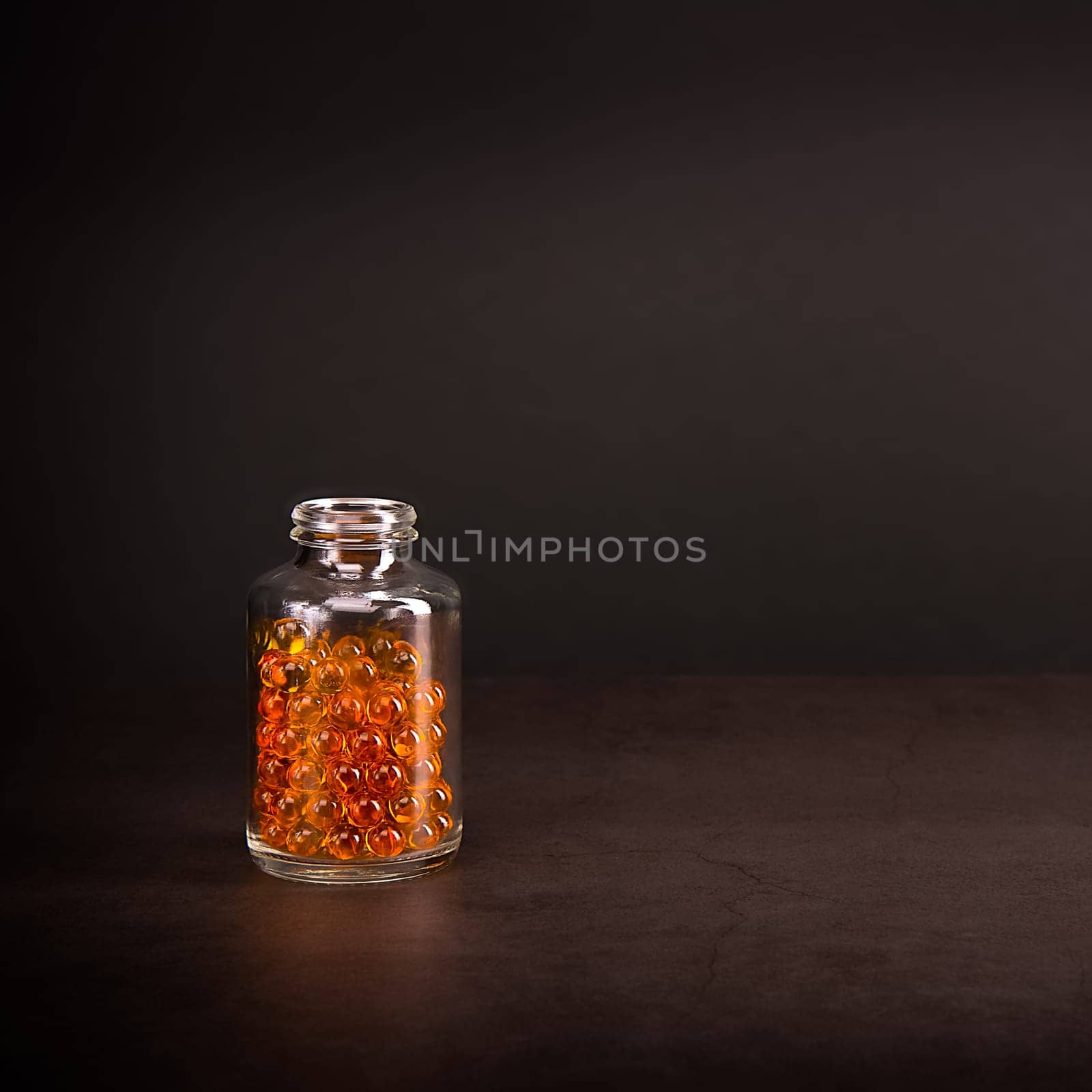 A glass jar with pills of bright orange yellow color on a brown background. Place for the label, logo, layout.