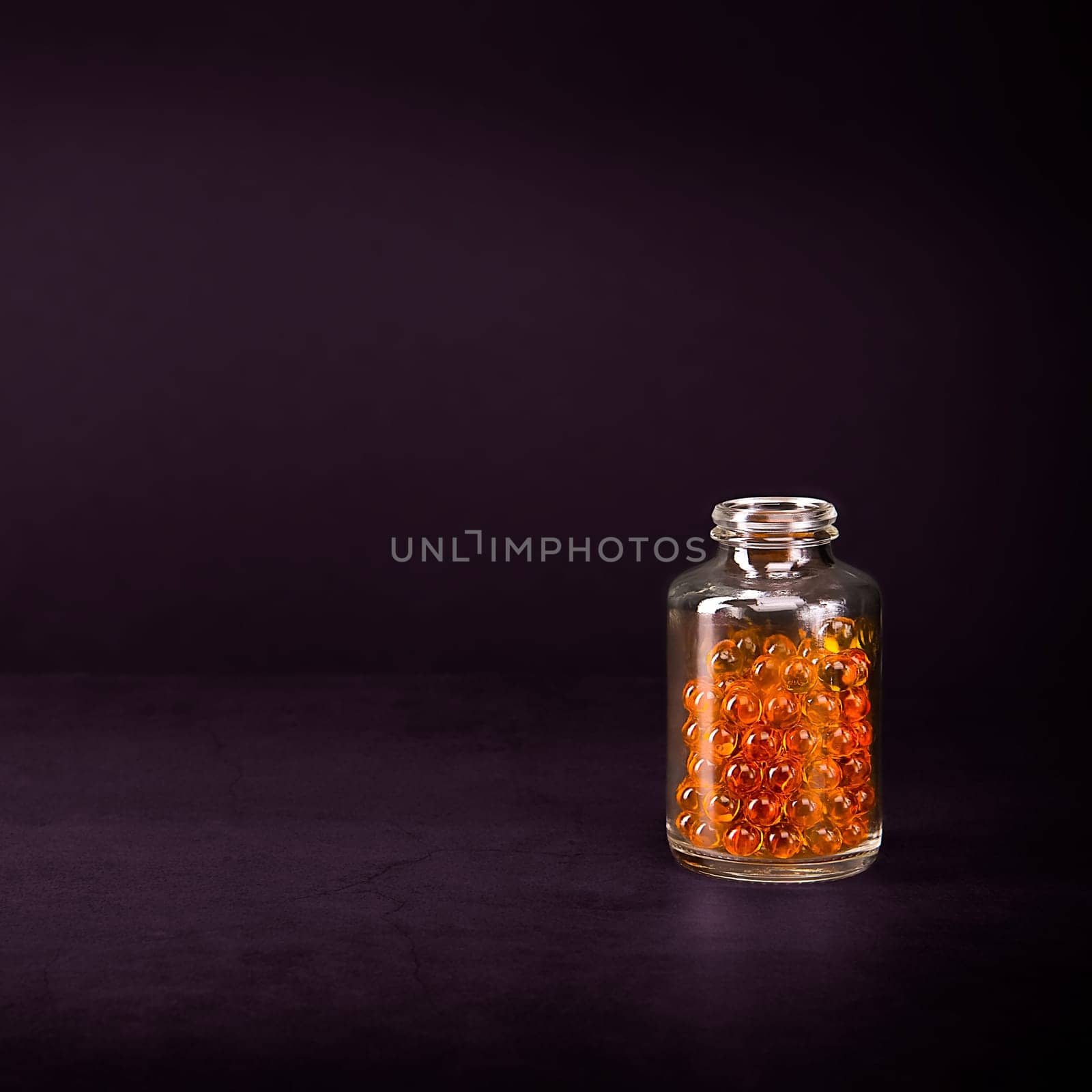 A glass jar with pills of bright orange yellow color on a lilac background. Place for the label, logo, layout.