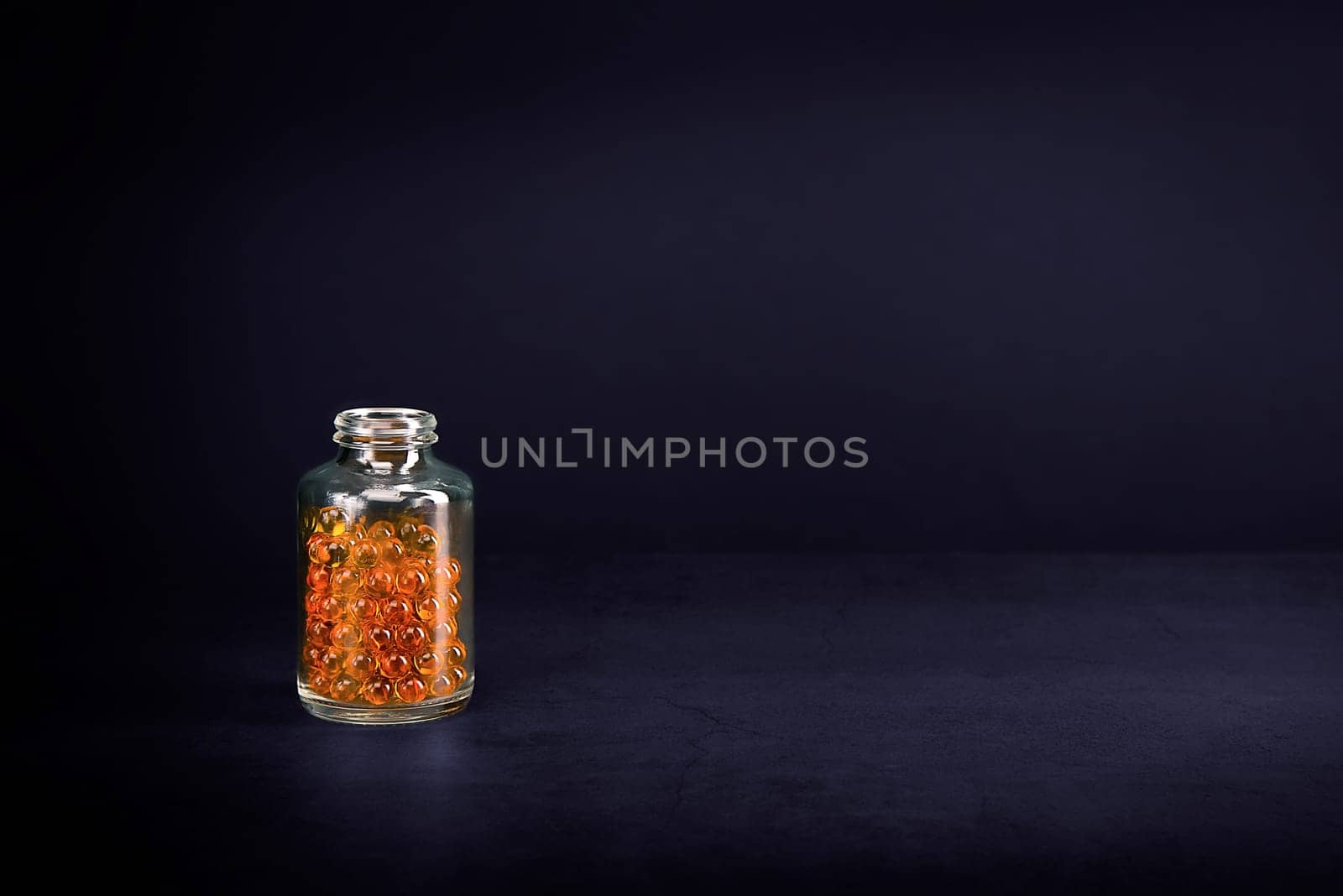 A glass jar with pills of bright orange yellow color on a purple background. Place for the label, logo, layout.