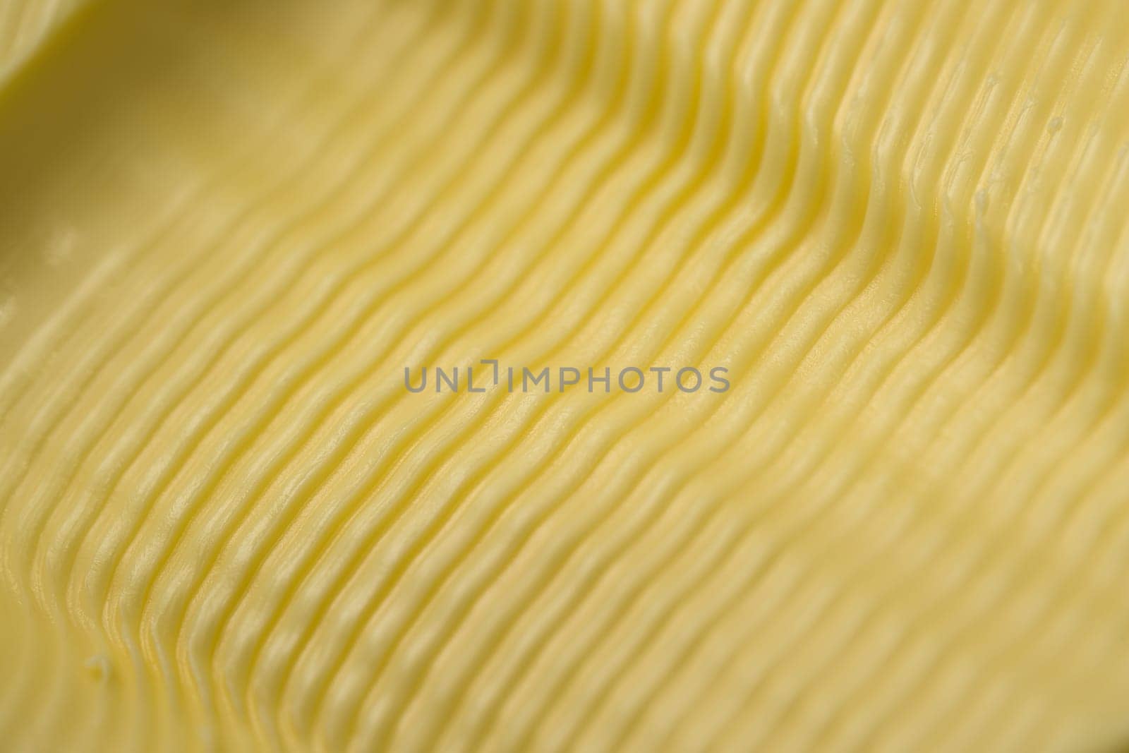 Wavy ripple pattern in butter created by a serrated butter knife. Full frame abstract food texture background, taken as a super macro close up.