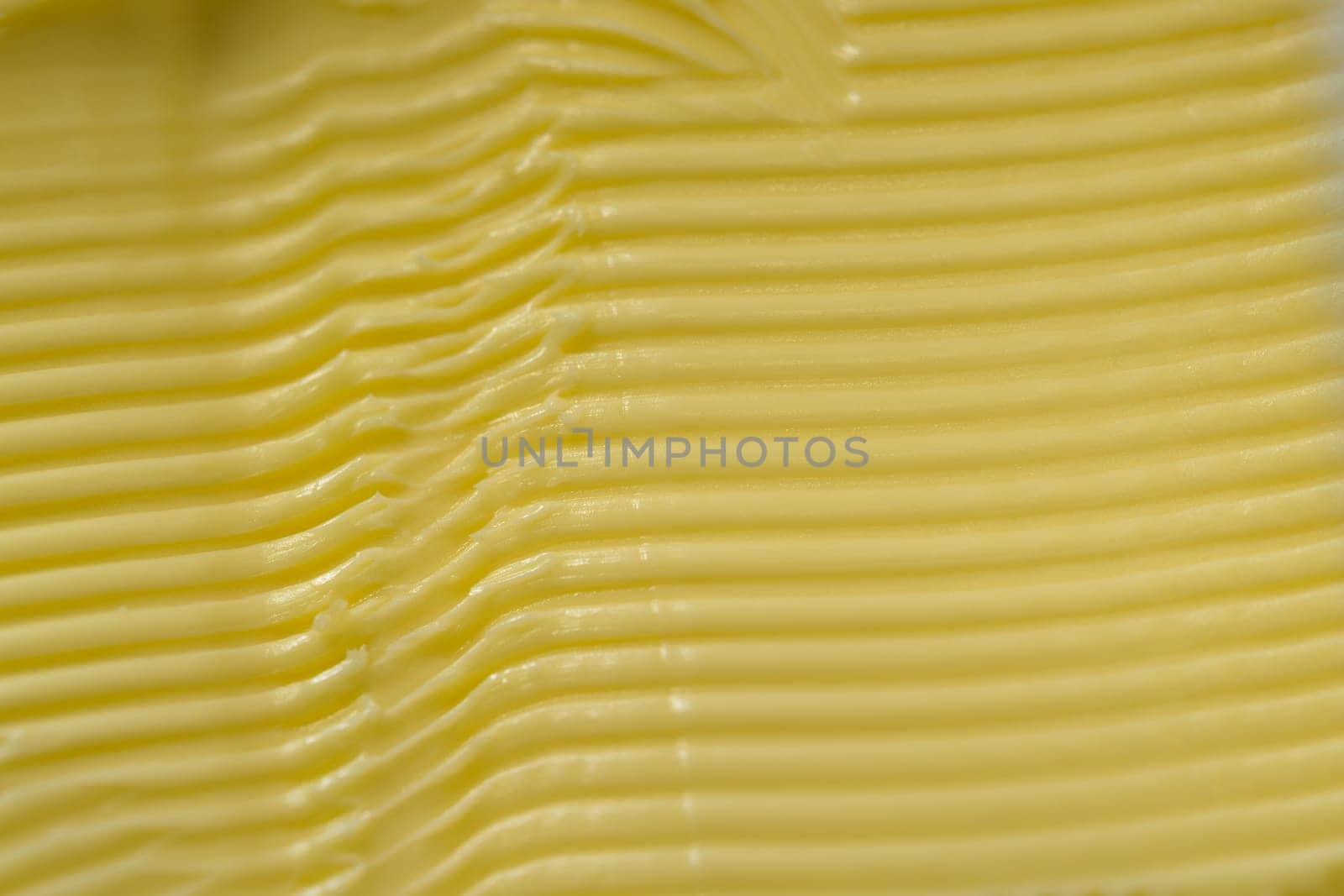 Super macro image of spreadable yellow margarine, after having a kitchen knife run through it to create a texture of horizontal grooves and ridges