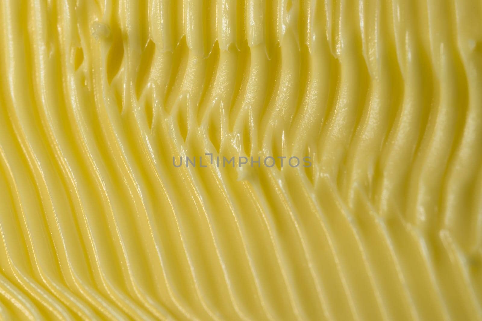 Food themed background of margarine. Shaped into detailed yellow grooves by a serrated kitchen knife used to spread it on bread. Full frame texture.