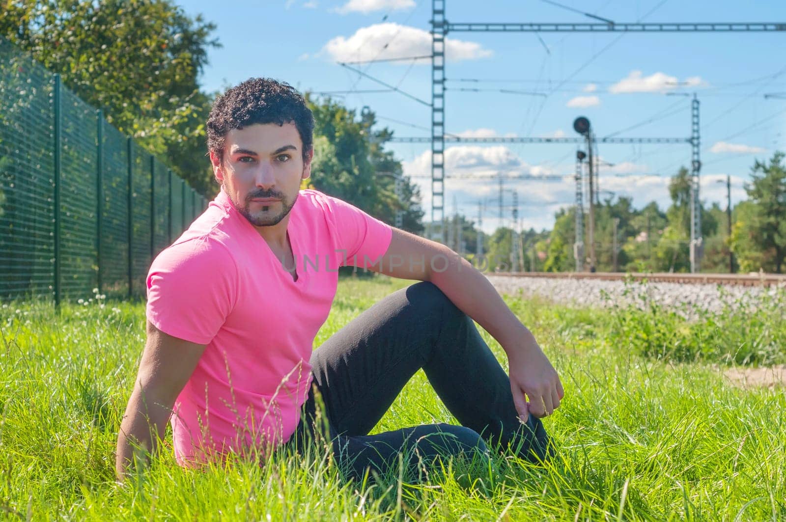 Young guy an in orange sitting on the grass near railway