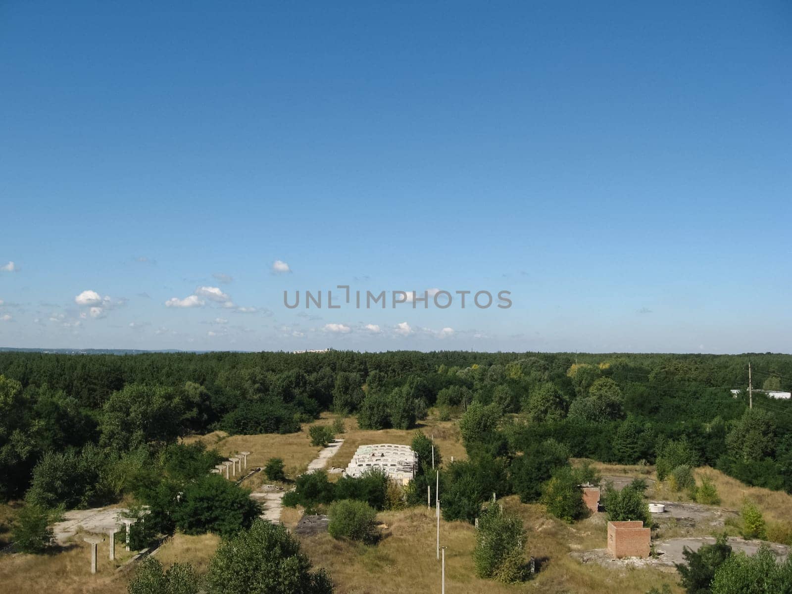 View from above on the site with old destroyed buildings, overgrown grass and trees.