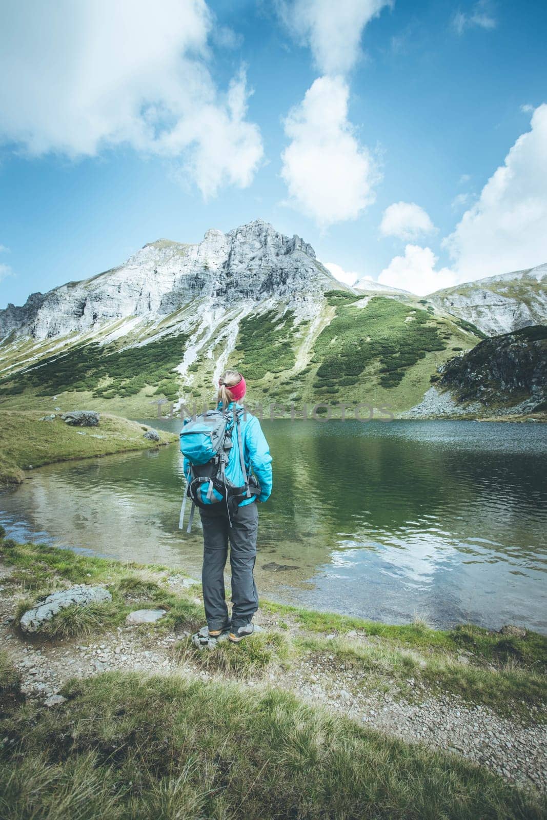 Female blonde mountain climber with backpack is enjoying the view