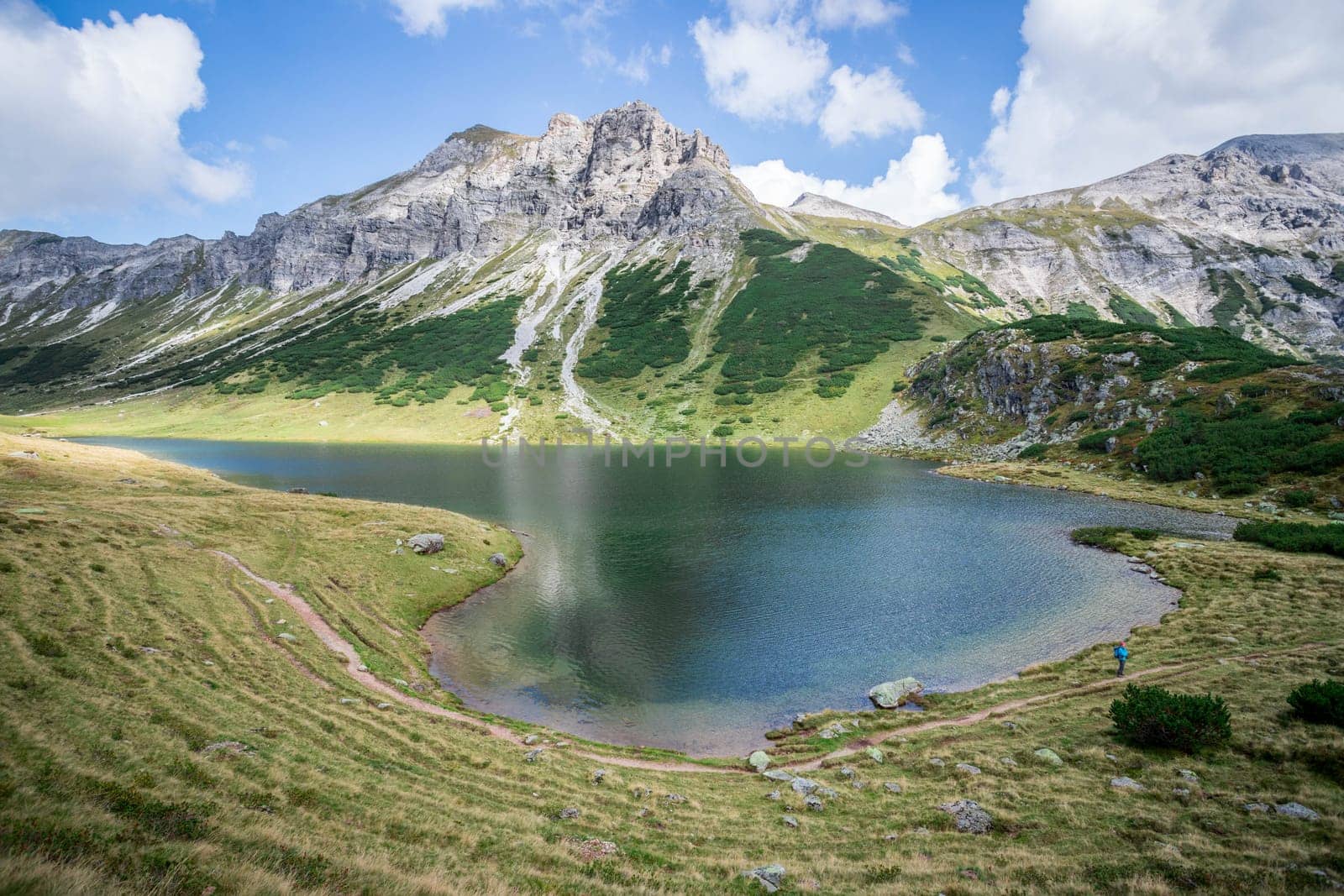 Mountain landscape: Rocky mountain range, clear water lake and blue cloudy sky
