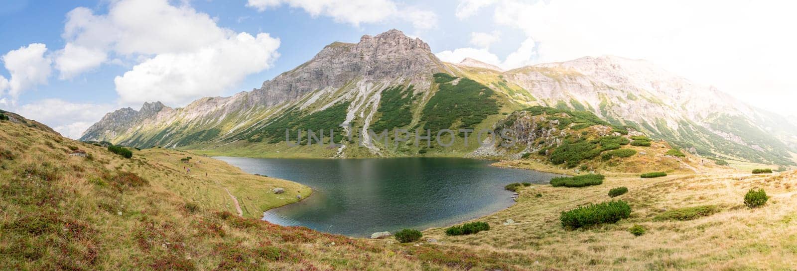 Mountain landscape: Rocky mountain range, clear water lake and blue cloudy sky  Panorama