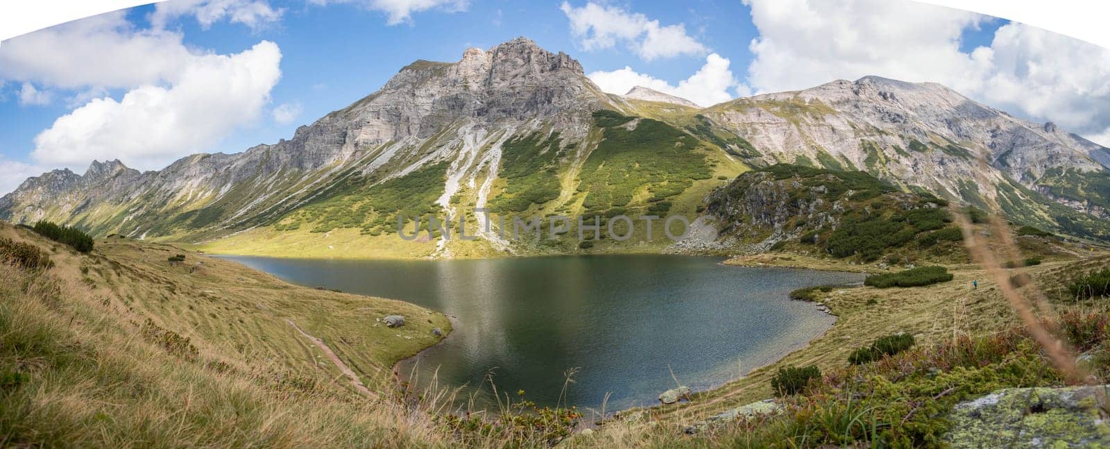 Mountain landscape: Rocky mountain range, clear water lake and blue cloudy sky