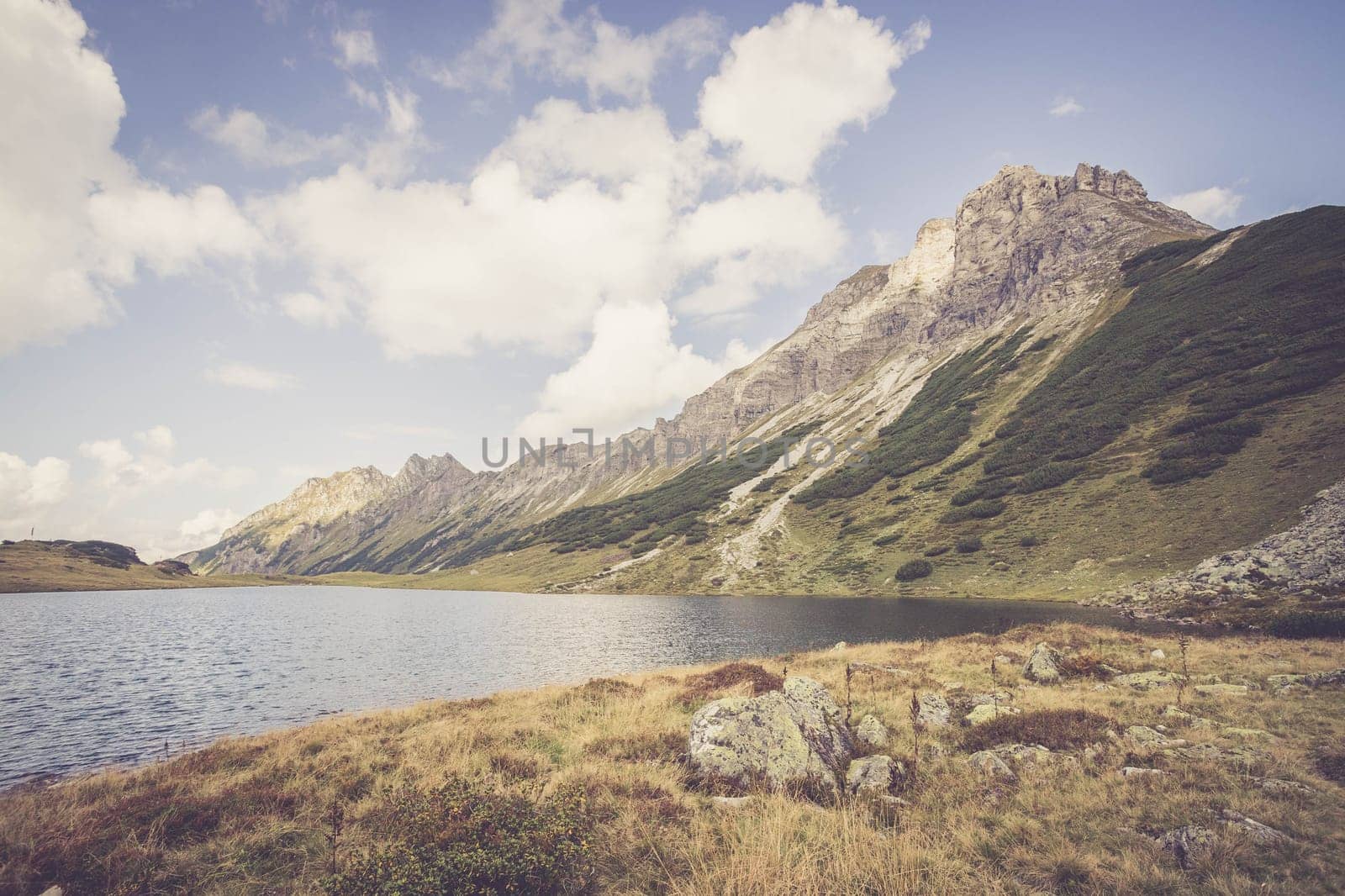 Mountain landscape: Rocky mountain range, clear water lake and blue cloudy sky