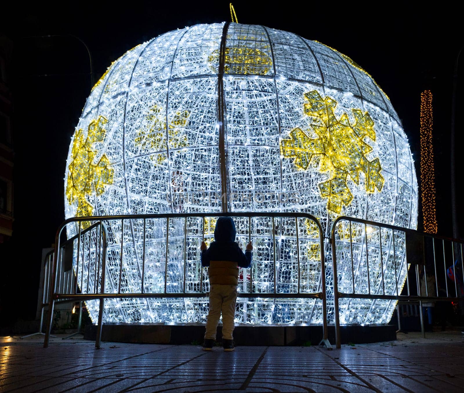 Little boy in front of Christmas led light balls decoration. He grabs a mobile fence placed all around the ball