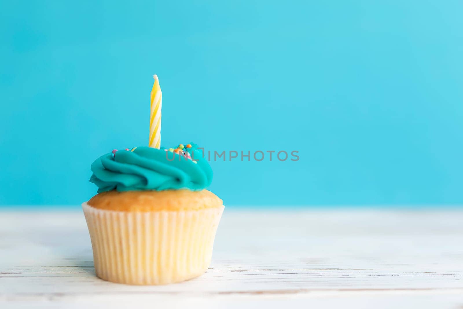 Birthday greetings concept. Yellow candle on a muffin or cupcake. Blue background. Wooden table