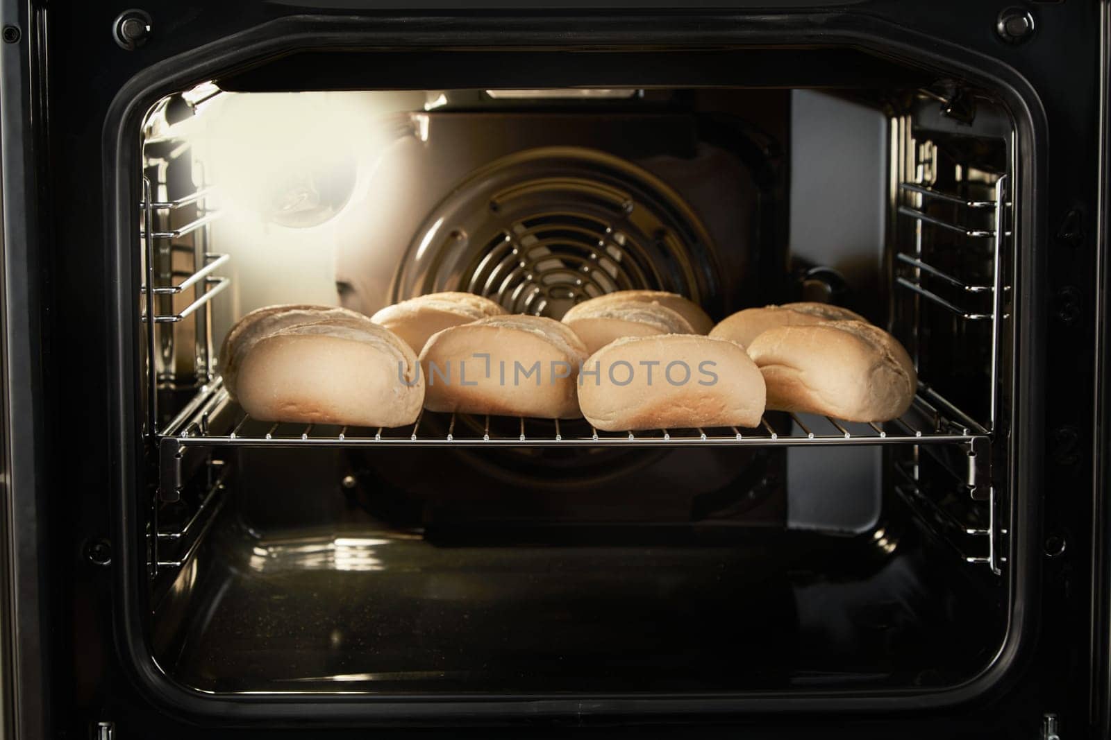Metal rack with half baked bread buns loaded in modern fan oven for baking