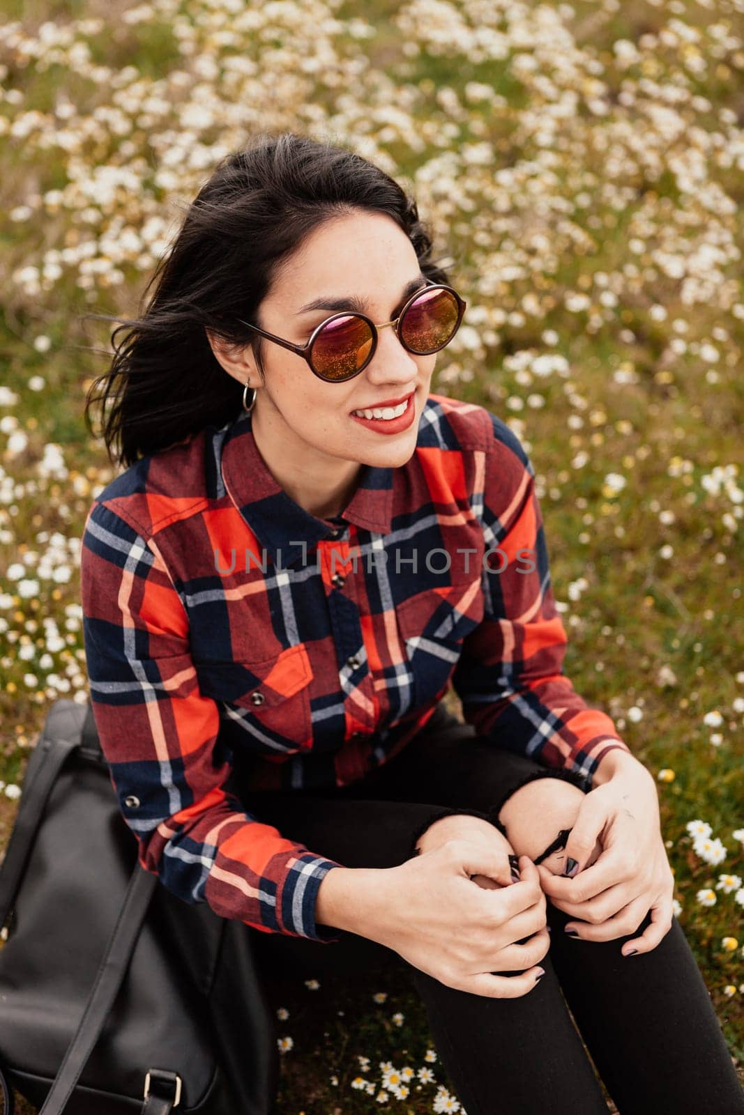 Beautiful woman with sunglasses sitting in the middle of a flowery meadow