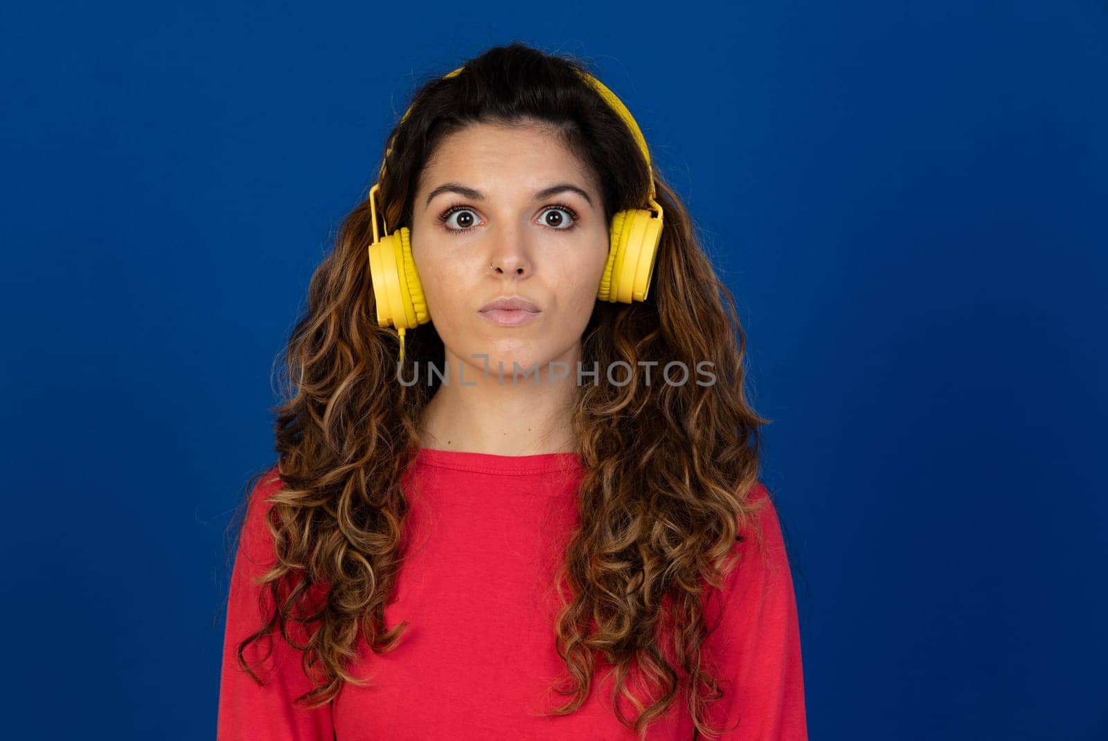 Portrait of beautiful caucasian girl with curly hair and headphones listening music isolated on a white background