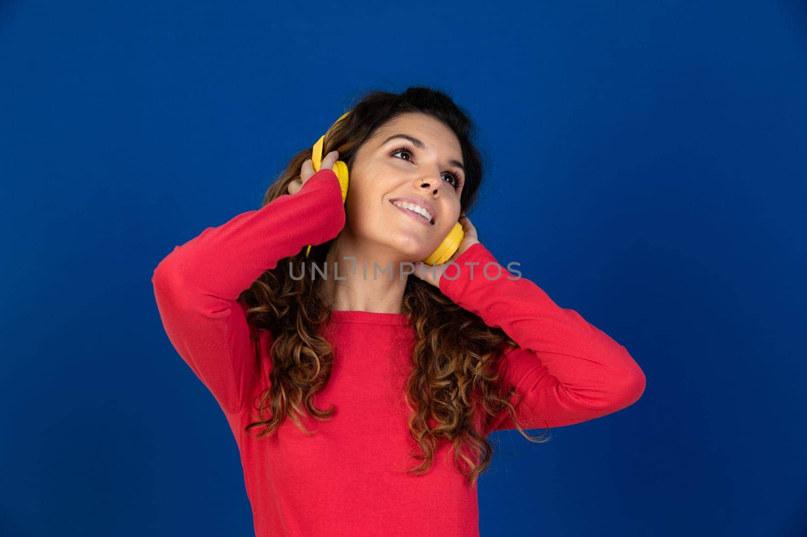 Portrait of beautiful caucasian girl with curly hair and headphones listening music isolated on a white background