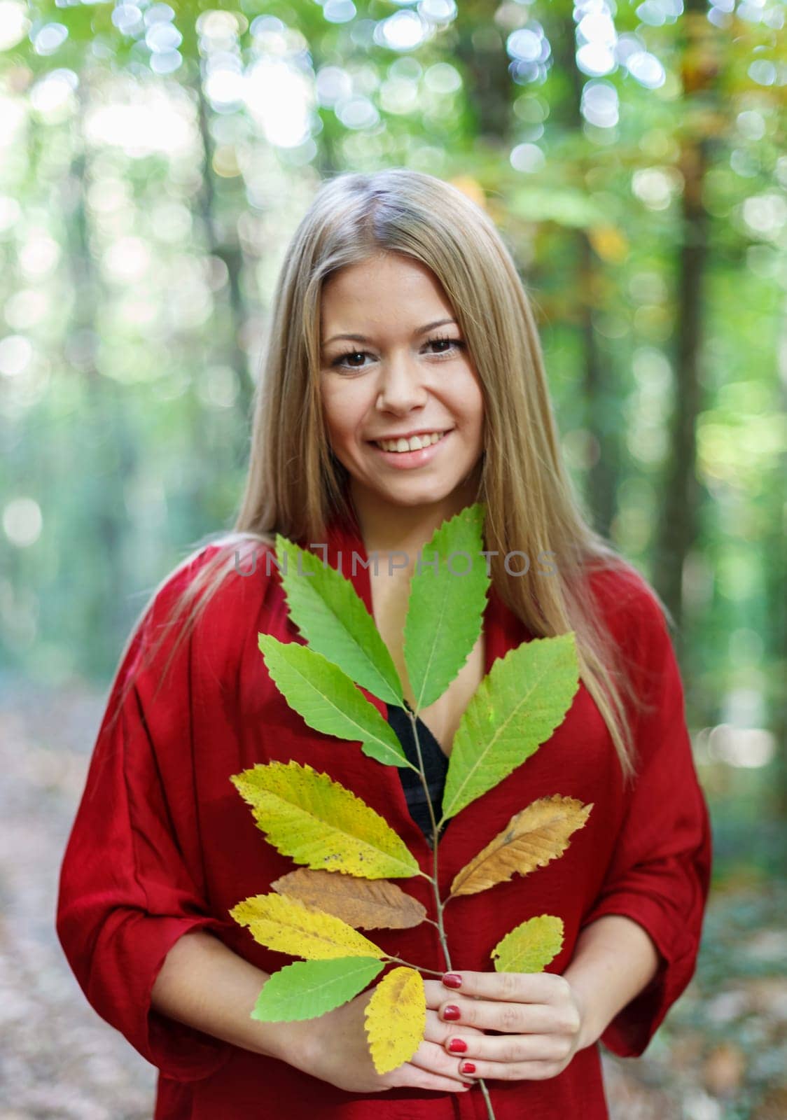 Blonde girl in a misterious forest holding a branch of a tree with autumn colors