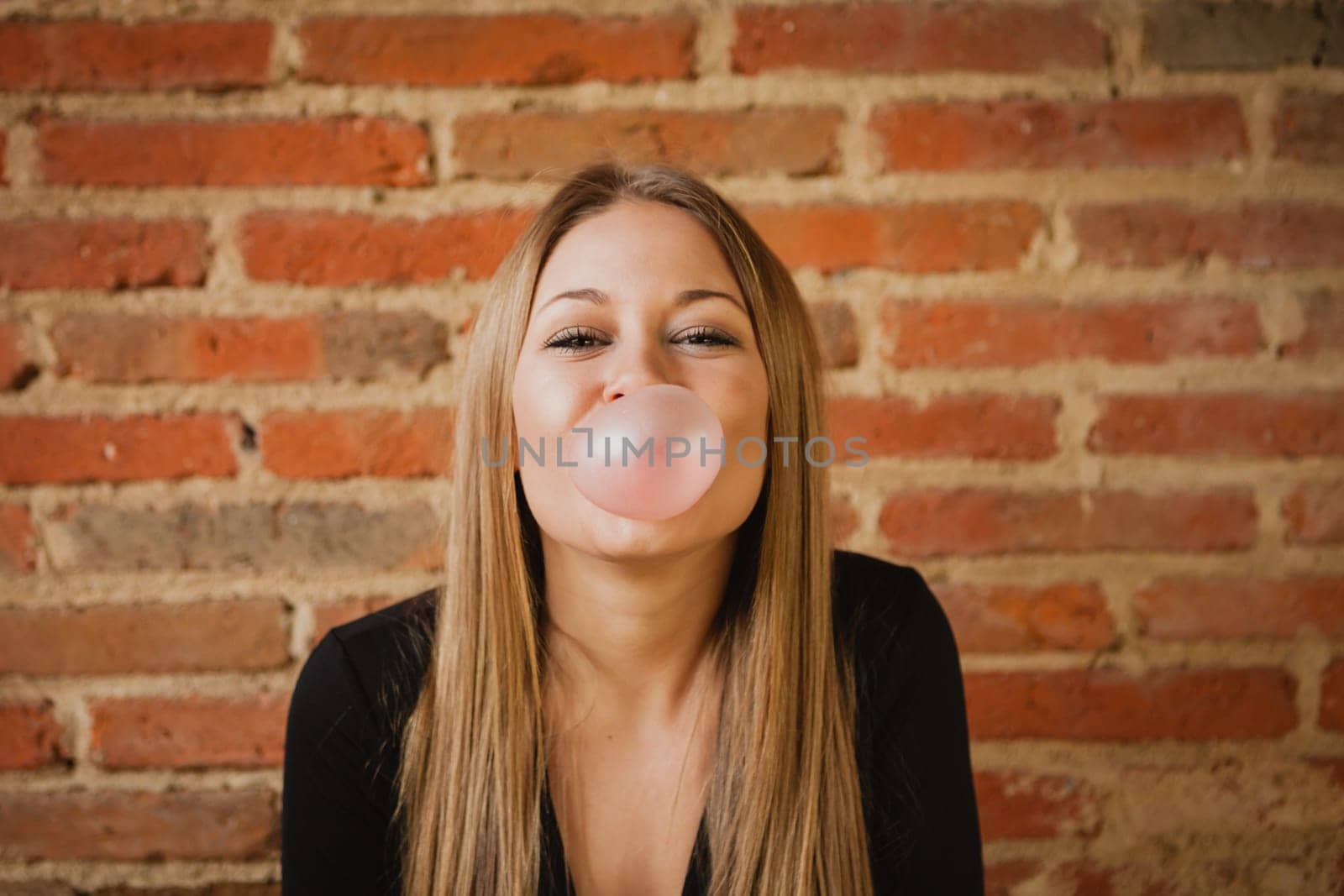 Funny girl making a pomp with a bubble gum and a brick wall of background