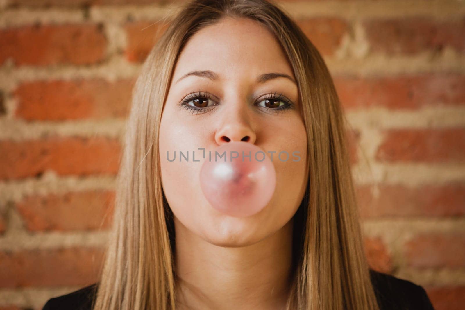 Funny girl making a pomp with a bubble gum and a brick wall of background