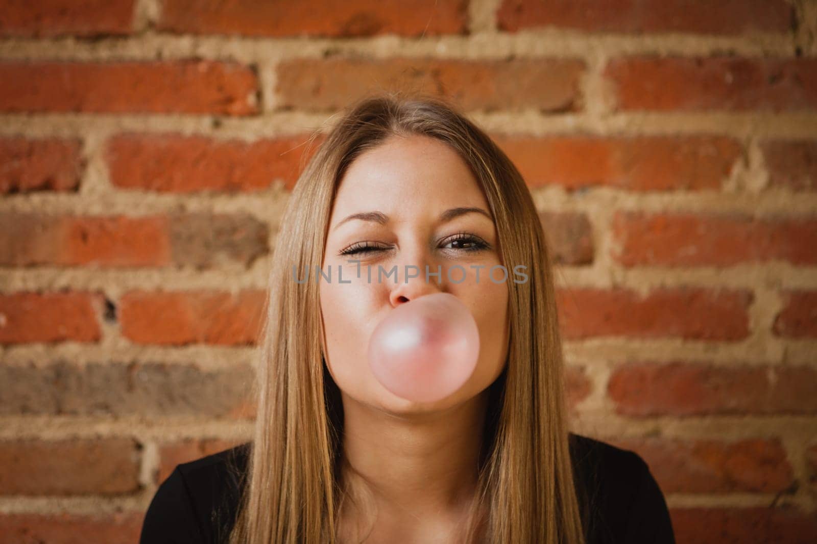 Funny girl making a pomp with a bubble gum and a brick wall of background