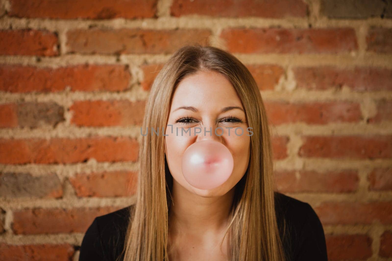Funny girl making a pomp with a bubble gum and a brick wall of background