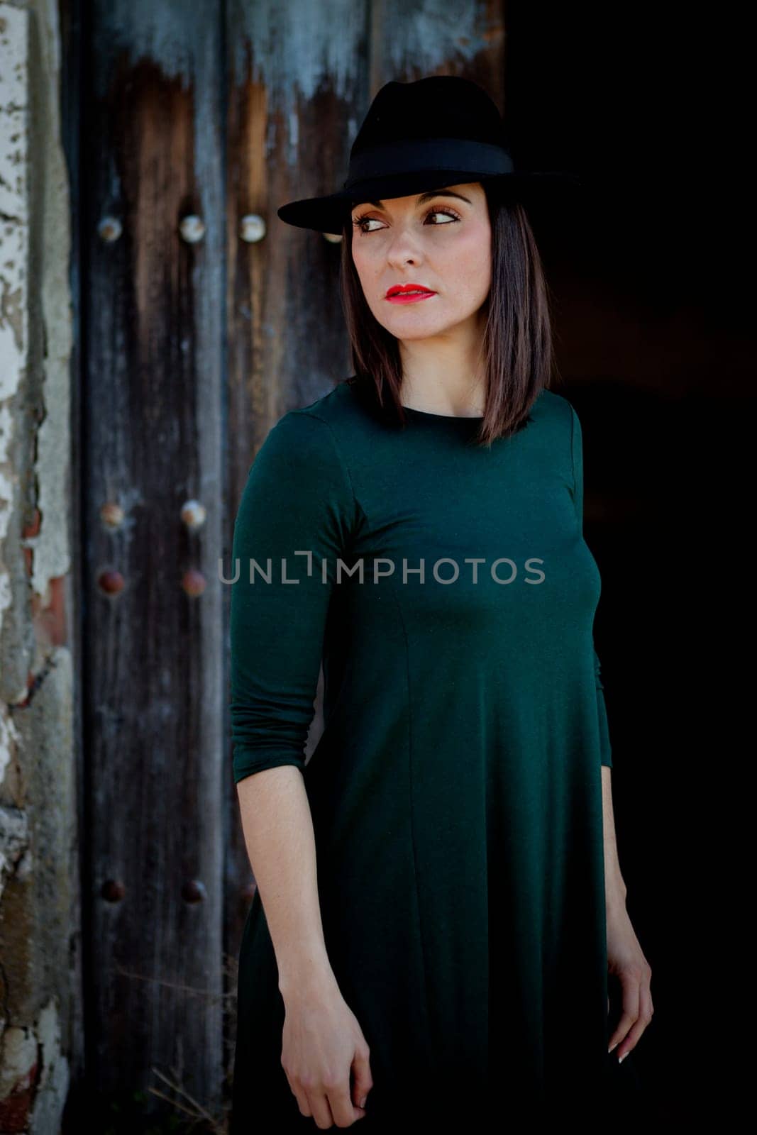 Pretty brunette girl in black with a stylish hat and a old wooden door of background