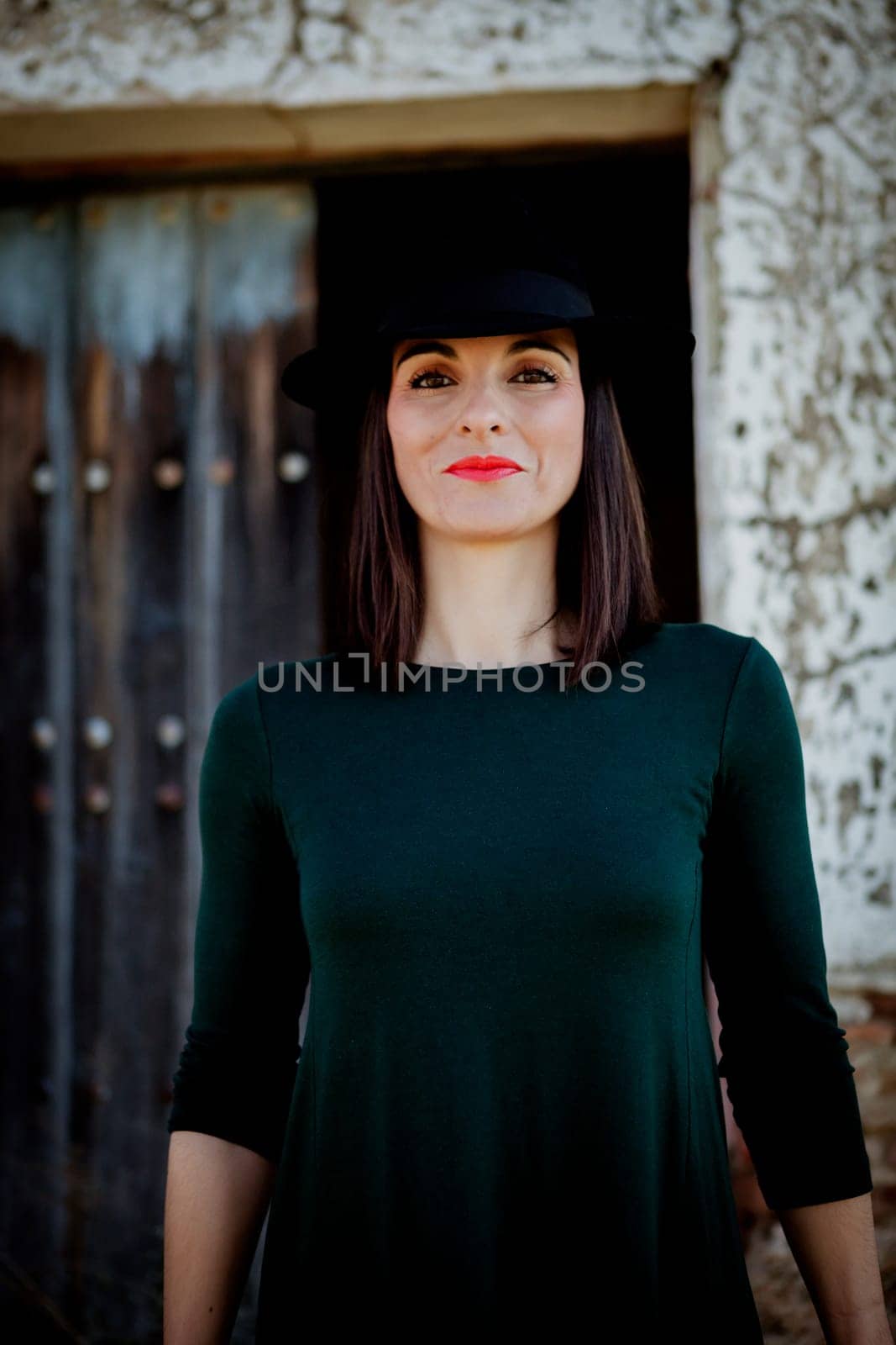Pretty brunette girl in black with a stylish hat and a old wooden door of background