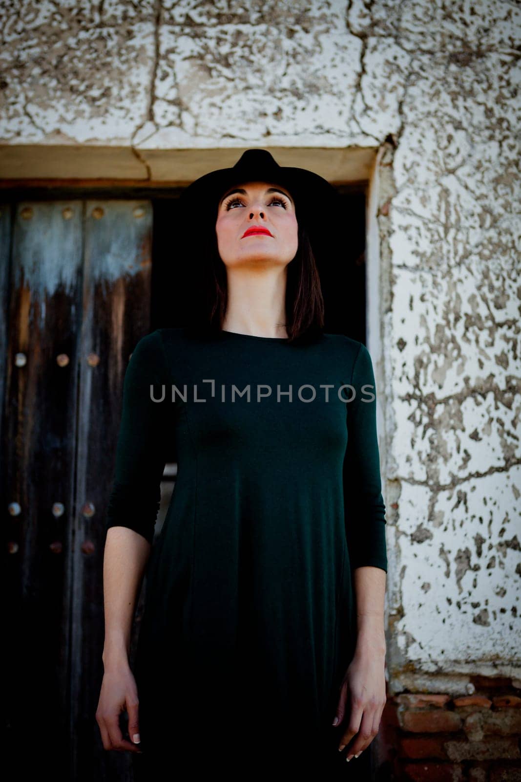 Pretty brunette girl in black with a stylish hat and a old wooden door of background