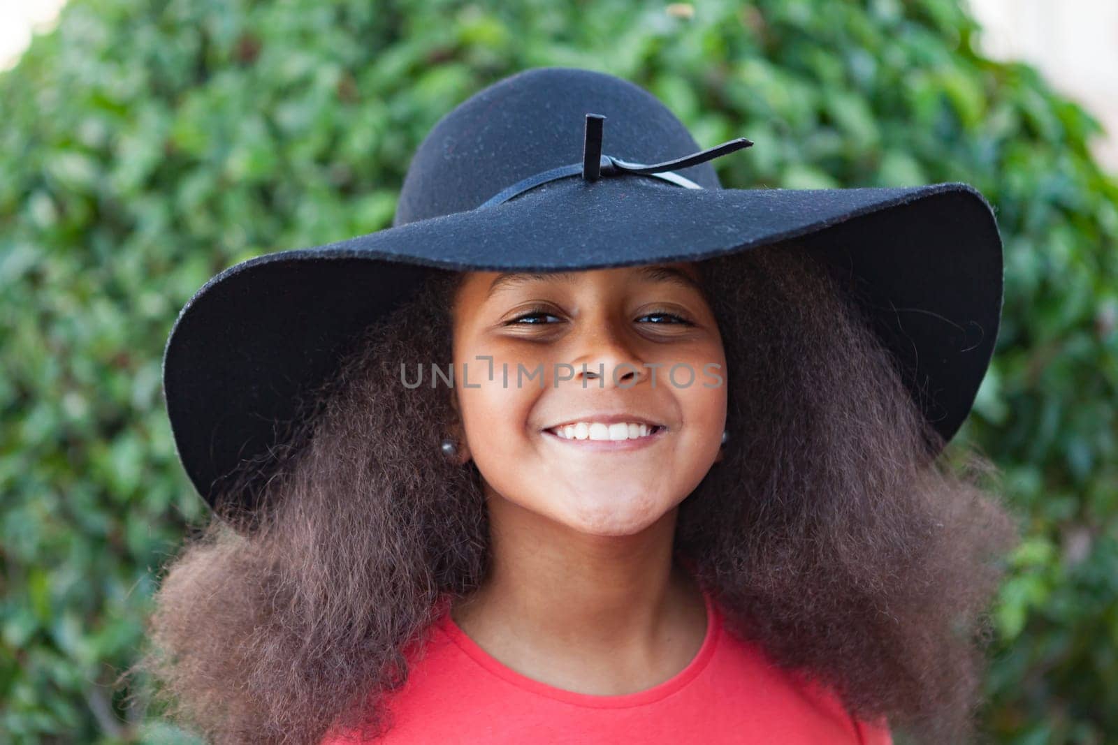 Pretty girl with long afro hair in the garden with a elegant black hat