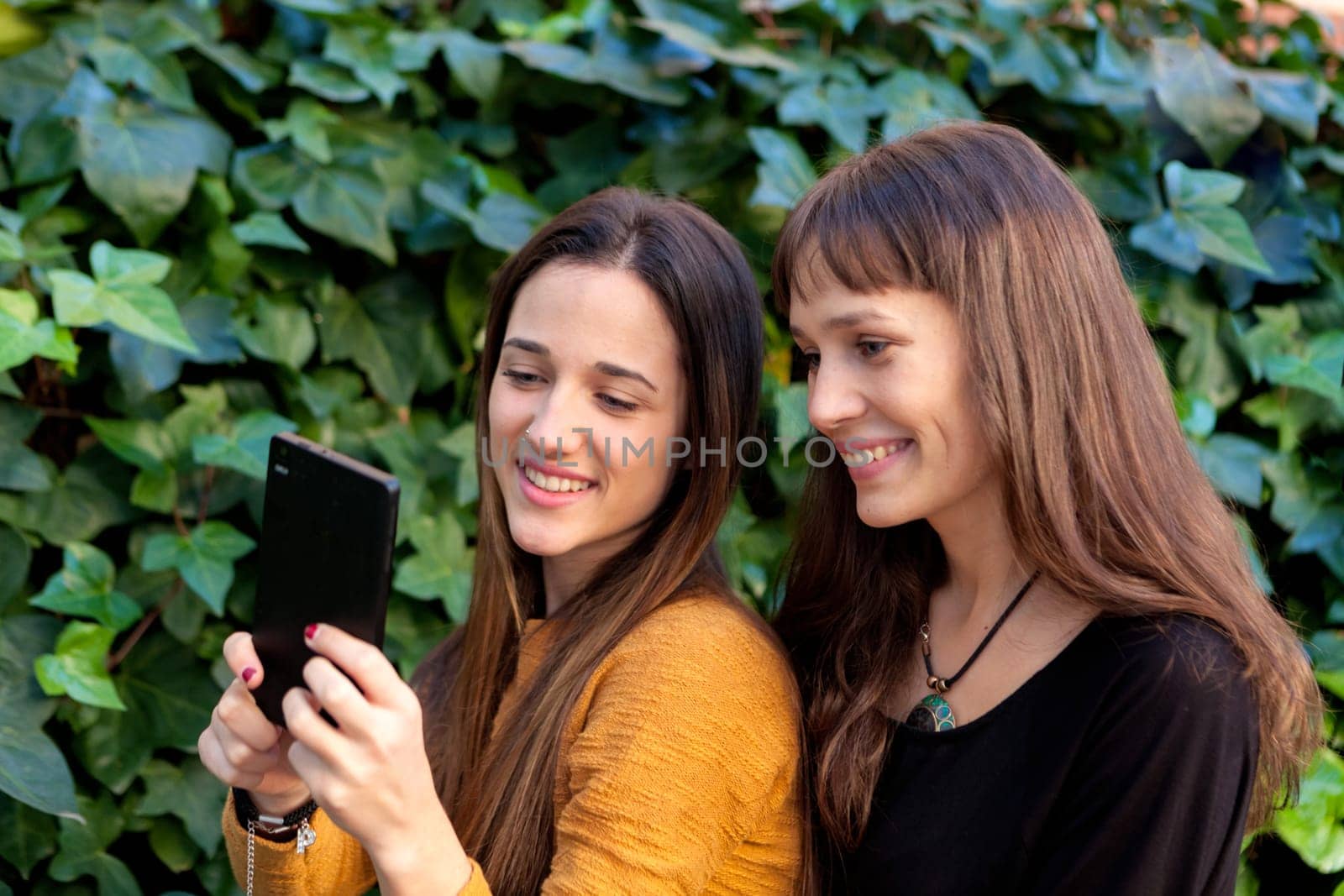 Two sisters enjoying of a day in the park with a mobile