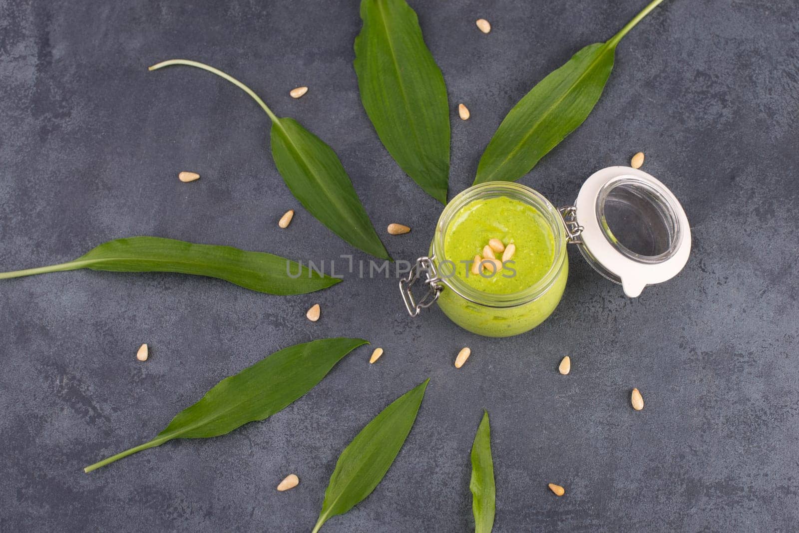 Pesto made from wild garlic, pine nuts and feta cheese in a glass, with fresh leaves on a dark textured background, empty space for text