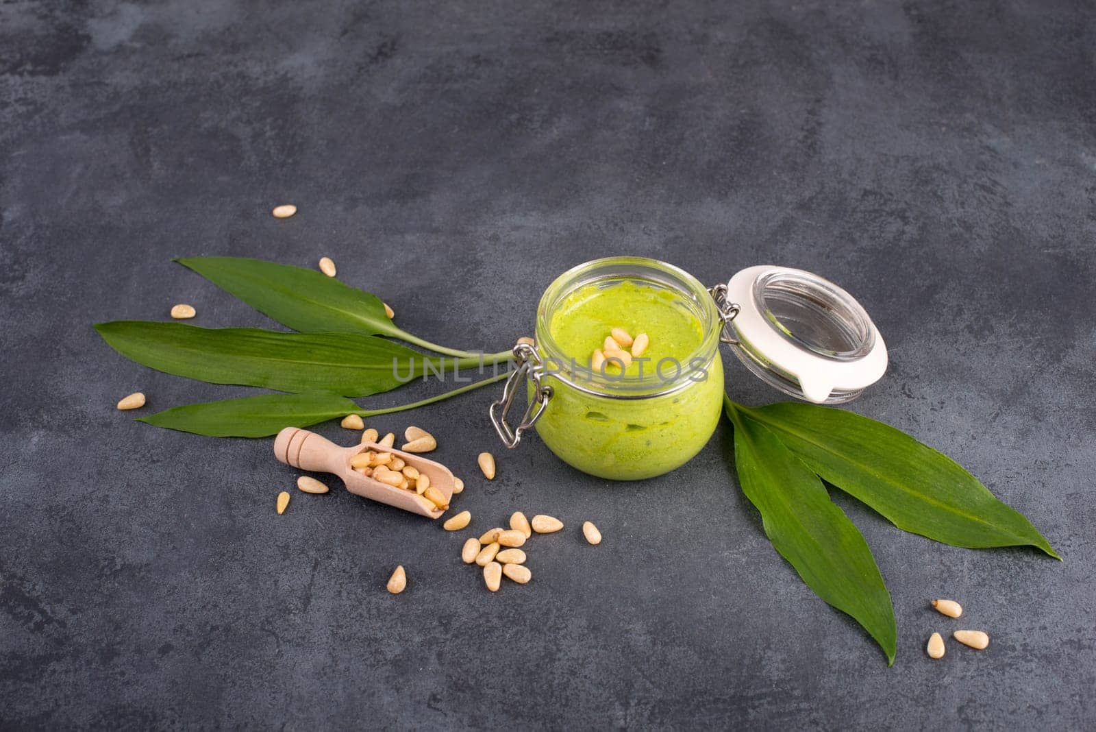 Pesto made from wild garlic, pine nuts and feta cheese in a glass, with fresh leaves on a dark textured background, empty space for text