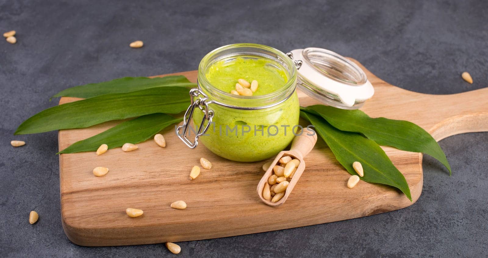 Pesto made from wild garlic, pine nuts and feta cheese in a glass, with fresh leaves on a dark textured background, empty space for text