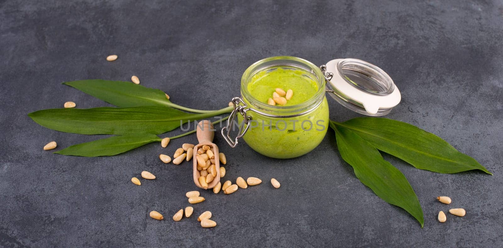 Pesto made from wild garlic, pine nuts and feta cheese in a glass, with fresh leaves on a dark textured background, empty space for text