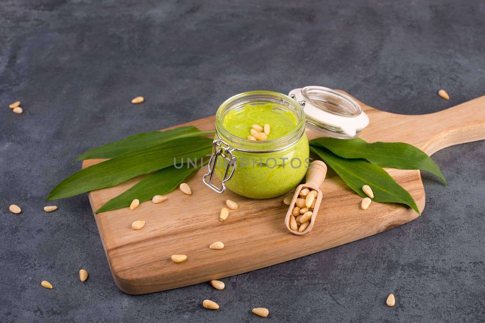 Pesto made from wild garlic, pine nuts and feta cheese in a glass, with fresh leaves on a dark textured background, empty space for text