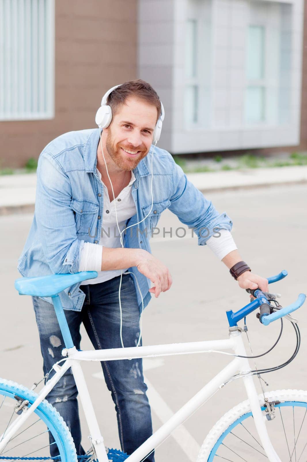 Casual guy next to a vintage bicycle listening music with headphones wearing denim shirt