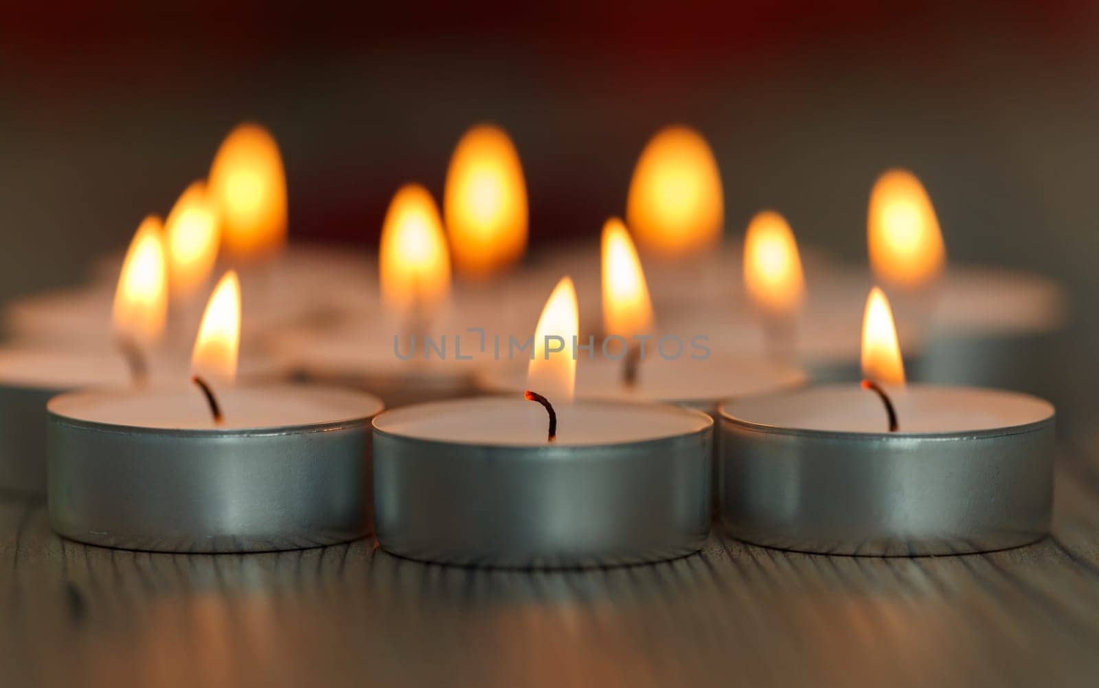 Many small burning candles on a wooden surface