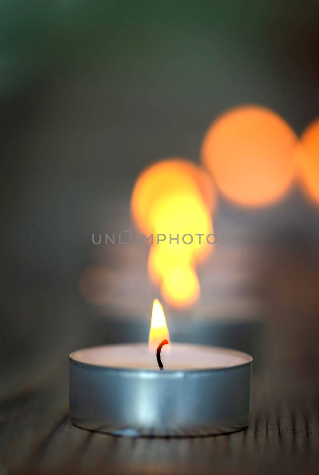 Many small burning candles on a wooden surface