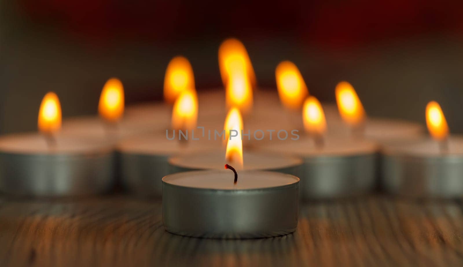 Many small burning candles on a wooden surface