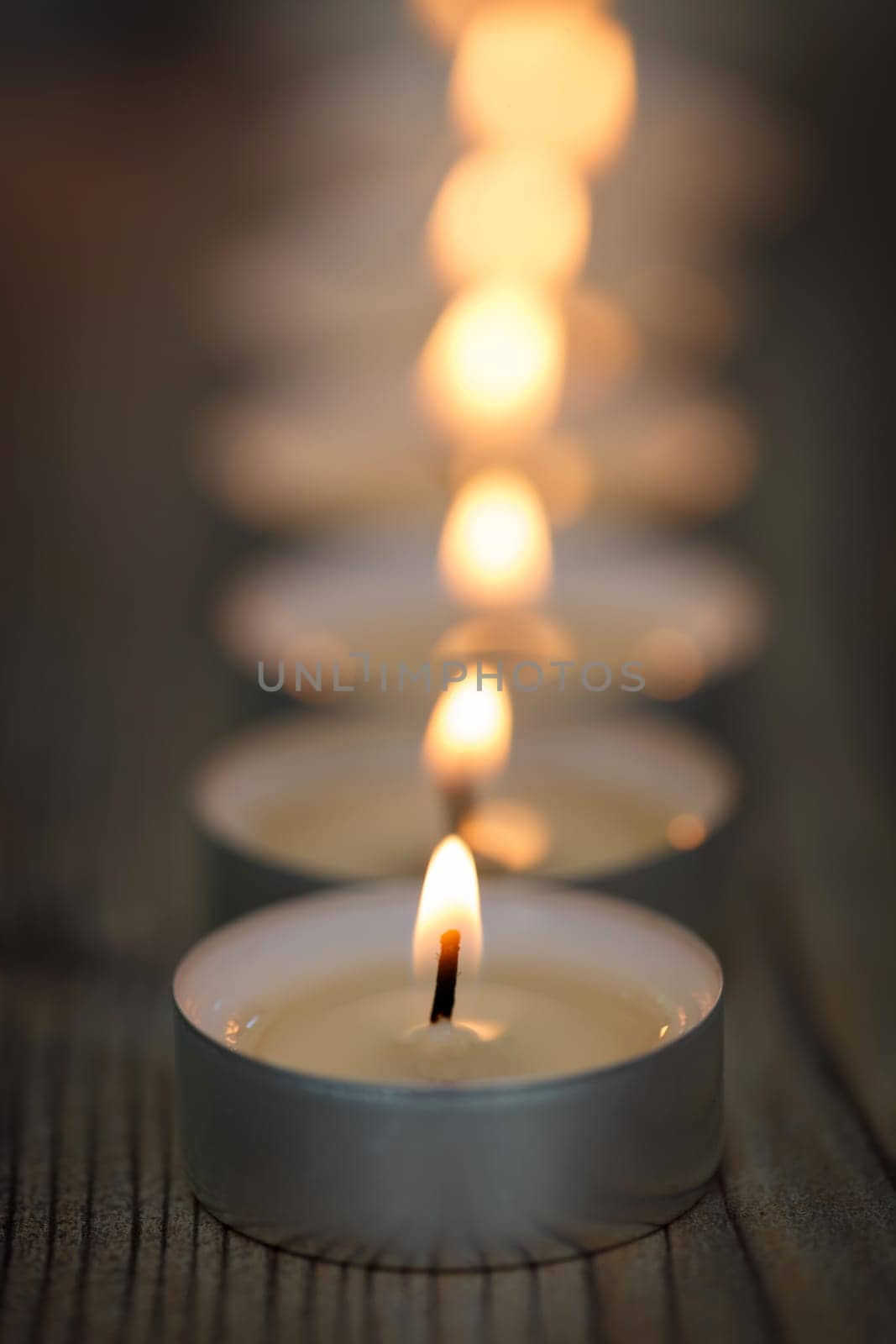 Many small burning candles in line on a wooden surface