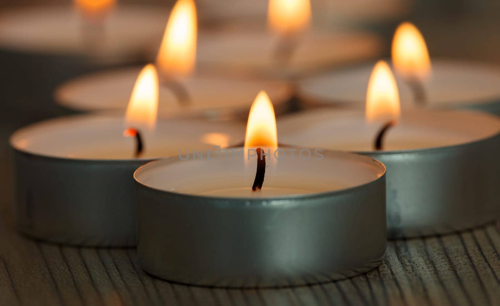 Many small burning candles on a wooden surface