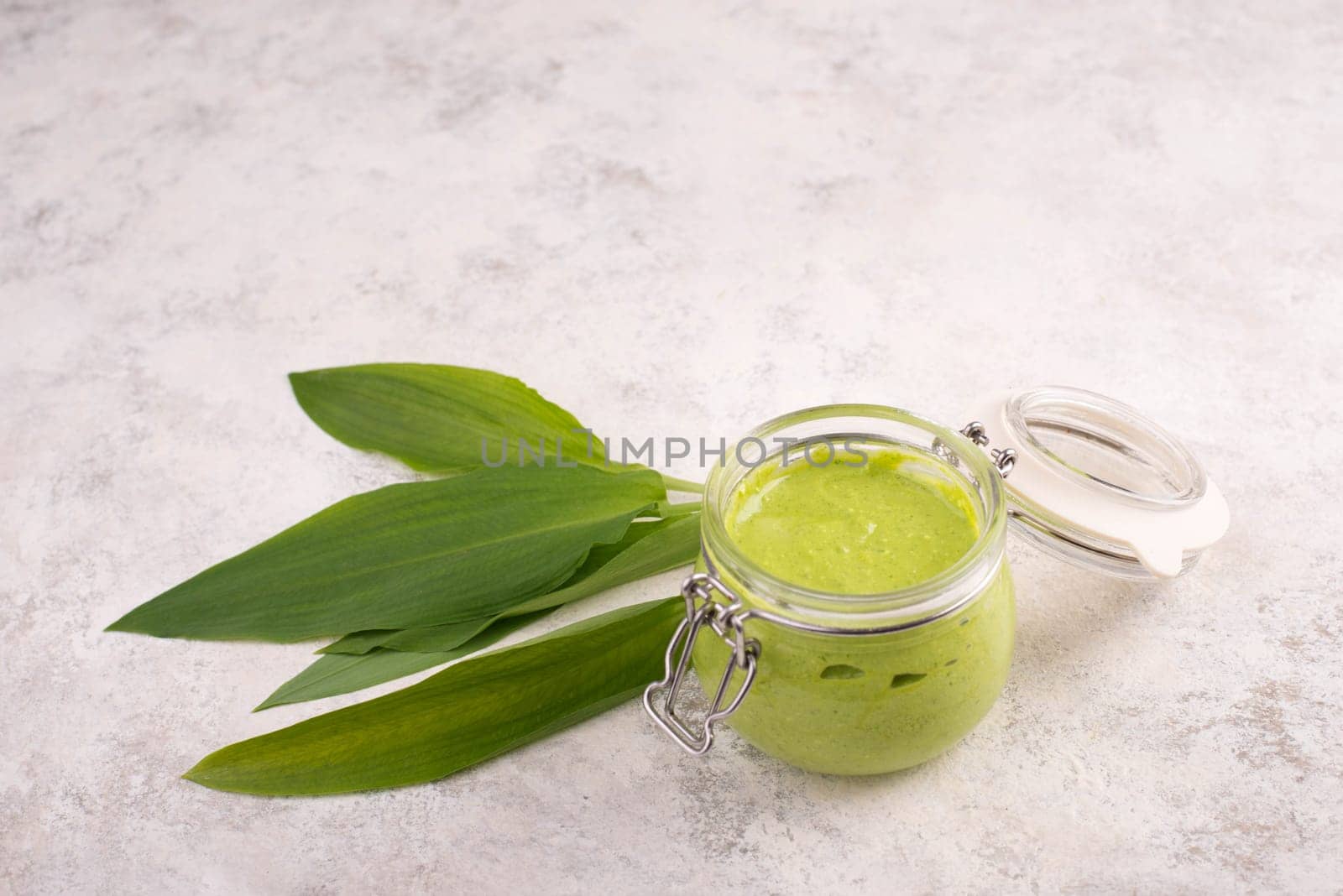 Pesto made from wild garlic, pine nuts and feta cheese in a glass, with fresh leaves on a textured background, empty space for text