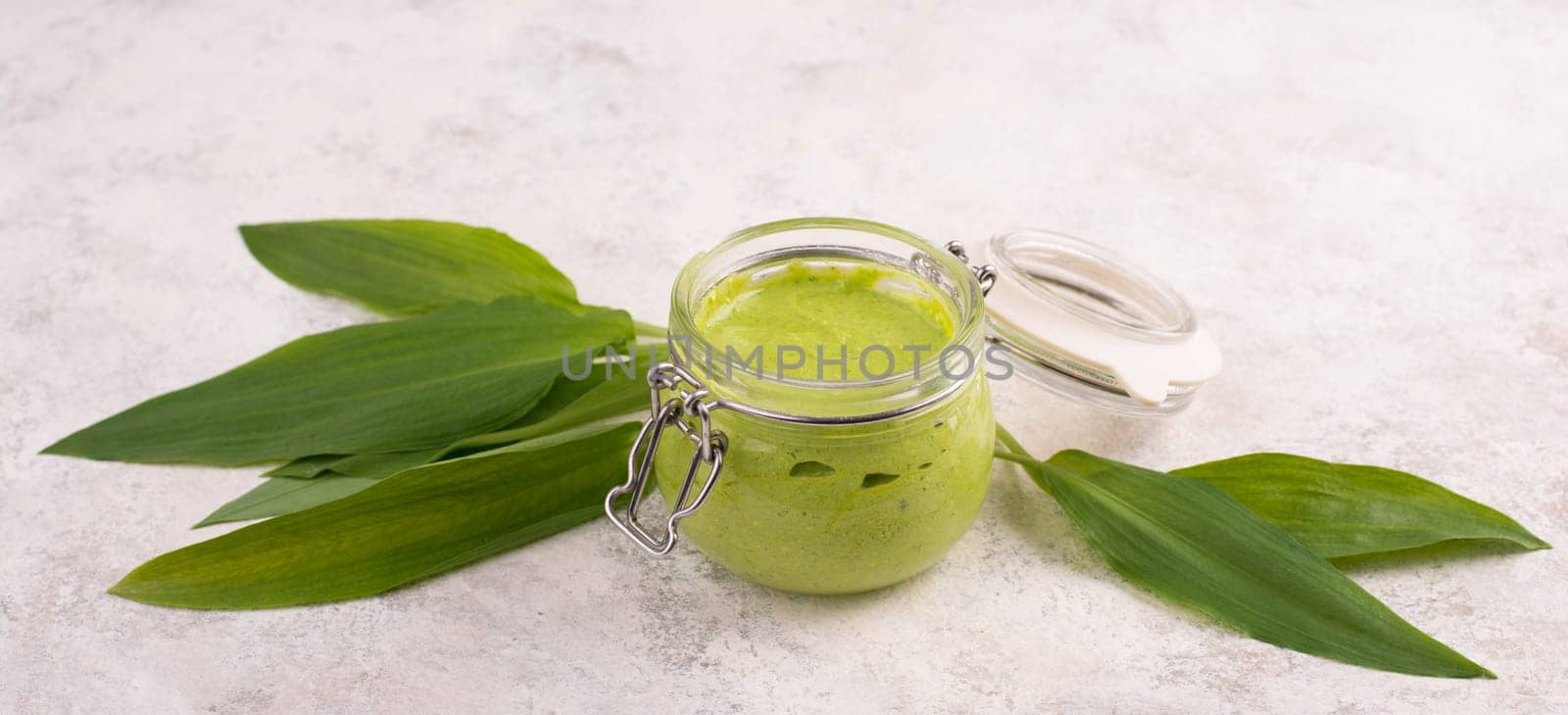 Pesto made from wild garlic, pine nuts and feta cheese in a glass, with fresh leaves on a textured background, empty space for text